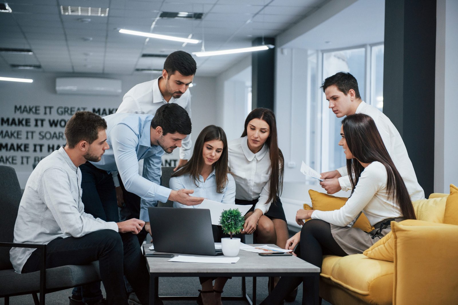 Guy shows document to a girl. Group of young freelancers in the office have conversation and working entorno profesional