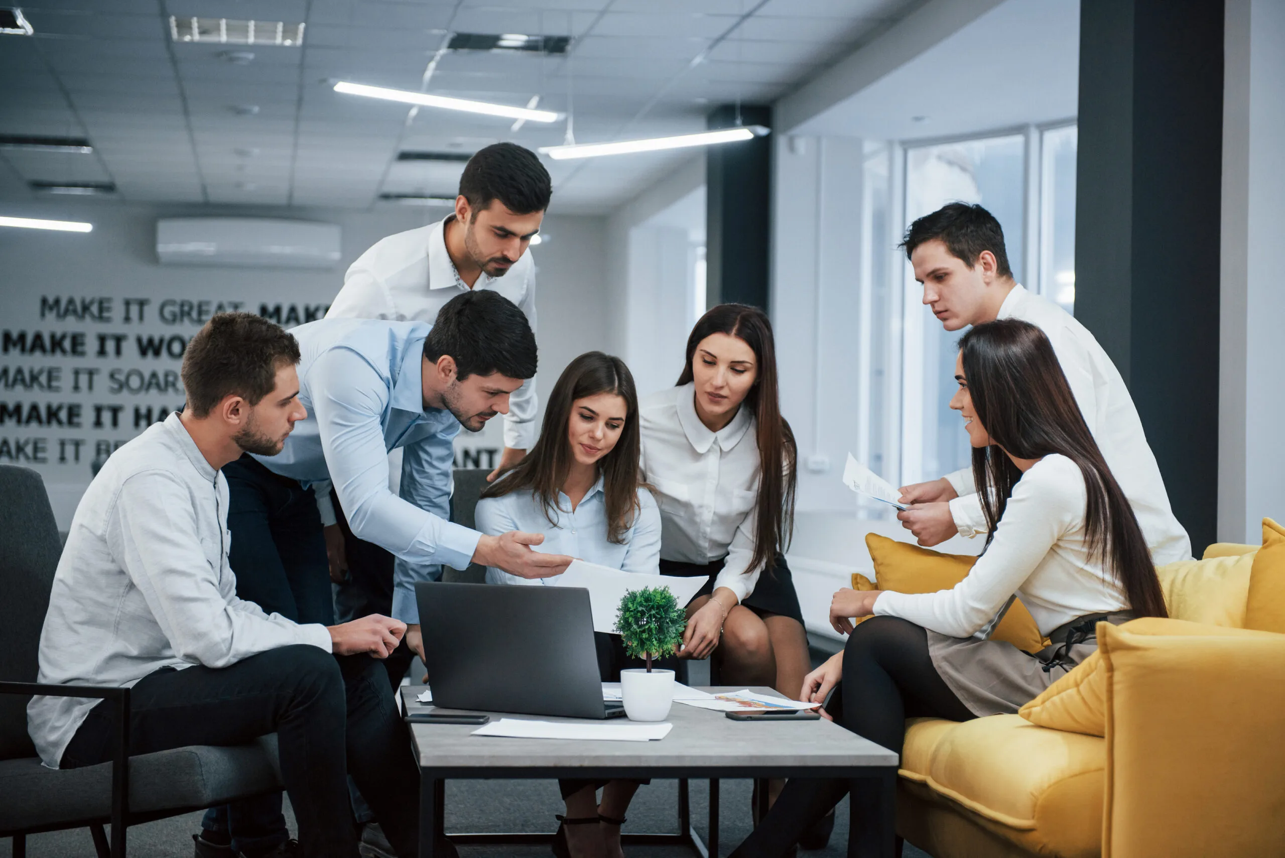 Guy shows document to a girl. Group of young freelancers in the office have conversation and working entorno profesional